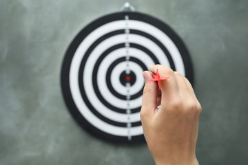 Woman throwing red arrow at dart board on grey background, closeup