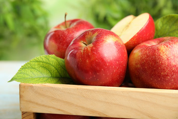 Wooden crate with ripe juicy red apples against blurred background, closeup