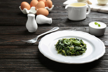 Plate with tasty cooked spinach on black wooden table. Healthy food