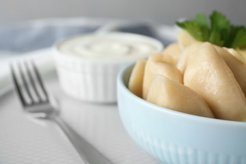 Delicious cooked dumplings and sour cream on table, closeup