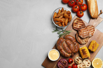 Flat lay composition with barbecued meat and vegetables on light table. Space for text