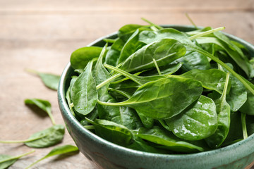 Bowl of fresh green healthy spinach on wooden table, closeup