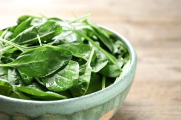 Bowl of fresh green healthy spinach on wooden table, closeup