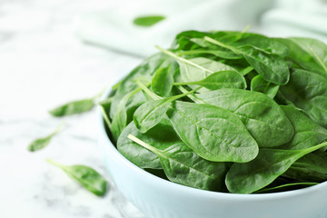 Bowl of fresh green healthy spinach on white marble table, closeup