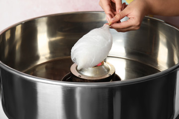 Young woman making cotton candy with modern machine on pink background, closeup
