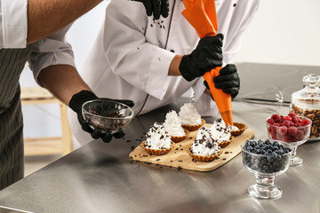 Pastry chefs preparing desserts at table in kitchen, closeup