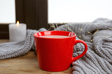 Cup of hot cocoa and sweater on window sill. Winter drink