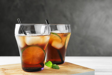 Glasses of refreshing iced tea on white table against grey background