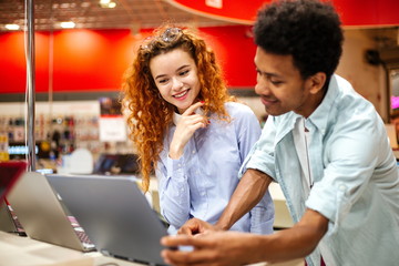 African man with redheaded girl standing in an electronics store picking out a laptop to buy