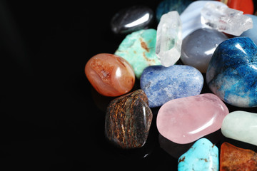 Different beautiful gemstones on black background, closeup. Space for text
