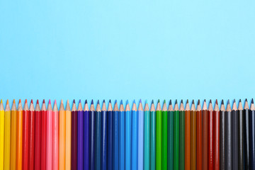 Colorful pencils on light blue background, flat lay. Space for text
