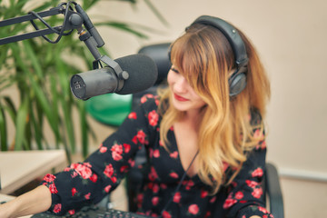 Obraz na płótnie Canvas Microphone in a radio broadcast studio. Blurred silhouette of a woman announces news in a radio studio