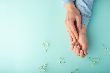 Flat lay. Tender female hands with white delicate flowers. On a turquoise background. Art photo, top view, horizontal photo.