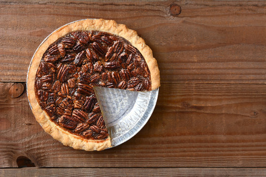 A Pecan pie with a slice cut out. Horizontal format on a rustic wood table with copy space.