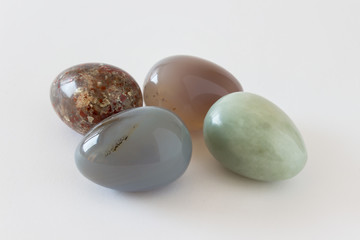 Four beautiful decorative Easter eggs made of glossy polished precious opal stones colored in dark brown green colors with inclusions on white background.