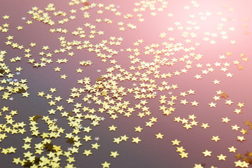 Abstract festive background with shiny randomly arranged golden stars on gray background. Photos with glow pink tint.