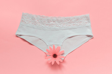 White elegant female lingerie underpants with a daisy flower on pink background.