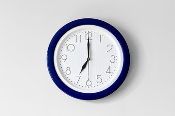 Large single round office clock showing seven o clock isolated on white background with blue detail and time arrows.