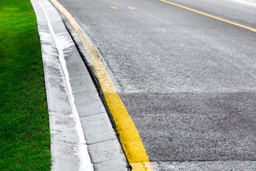 Fototapeta premium flowing rainwater in the canal is a cement ditch of a drainage system on the side of an asphalt road with yellow markings and a green lawn after rain on a overcast day.
