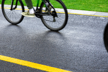 Fototapeta na wymiar asphalt bike path wet after rain with yellow markings with a passing black bike blurred in motion, sports background on a bicycle theme close up.
