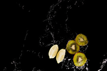top view of cut lemon and kiwi in clear water puddle isolated on black