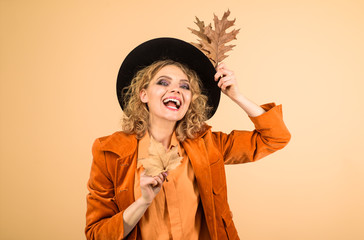 October. Beautiful model girl with autumnal leaves. Woman autumn fashion. Fall. Happy woman with autumn leaves in orange jacket. Fashionable woman with autumn leaves in hand. Autumn girl in black hat.