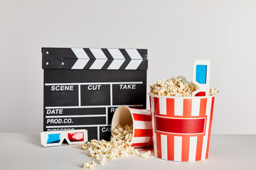 delicious popcorn scattered from buckets with clapper board and 3d glasses isolated on grey