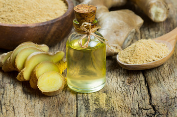 Glass bottle of essential ginger oil, ginger root and powder on wooden rustic background. Healthy...