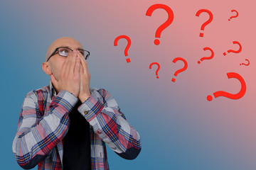 question marks around a young man with glasses covering his face with his hands, psychological concept