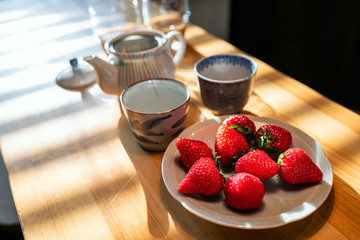 Traditional Japanese dessert plump expensive strawberries on plate at wooden table in kitchen with two teacups or cups and teapot with green tea