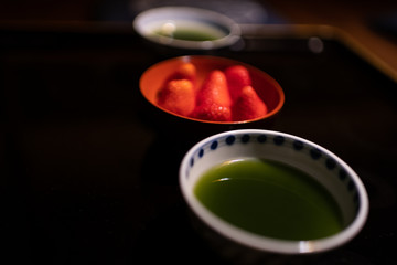Closeup of traditional Japanese dessert bowls cups with matcha green tea and strawberries in ryokan on black lacquered wood table