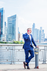 Young American Businessman with beard, talking on cell phone, traveling in New York City, wearing blue suit, white shirt, standing in business district with high buildings in Midtown of Manhattan..