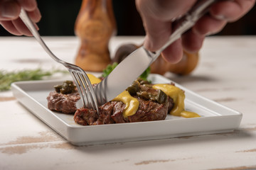 Filet mignon with caper and mustard sauce, broccoli, pepper grinder on wooden white background, soft light