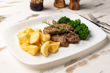 Beef stew with rustic potato and broccoli in a white plate on white wooden table background, soft light