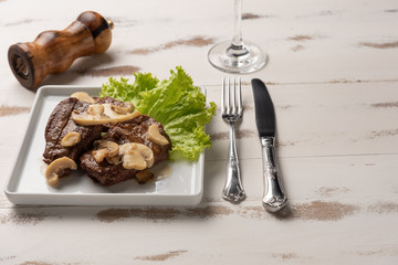 Filet mignon with mushroom sauce, lettuce, pepper grinder on wooden white background, soft light