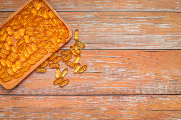 top view of nutritional supplement gold capsules in wooden plate on wooden table.