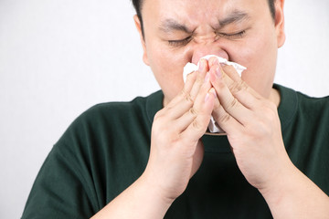 Close up of young Asian man gets sick and blows his nose with napkin. Sneezing, cold, flu virus, illness disease, health care and treatment concept.