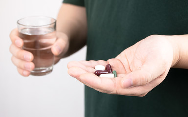 Close up photo of young man taking pill and holding a glass of water in hand. Health care, treatment, illness disease, supplements, vitamin and medicine concept.