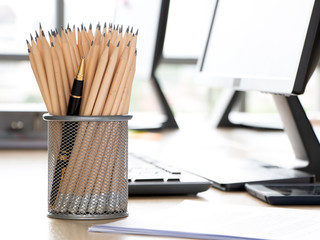 A pen standing out from the crowd of plenty pencil in a metal holder at modern office. Individuality, unique, independence, think different, initiative, leadership, business success concept.