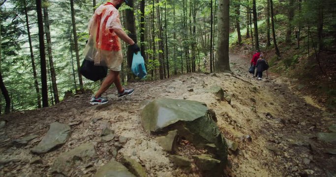 Ecology cleaner walking with rubbish bags on rocky hillside in the pine forest. Team of active young people fighting for ecology cleaning up nature landscape together.