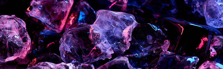 panoramic shot of clear ice cubes with purple colorful lighting isolated on black