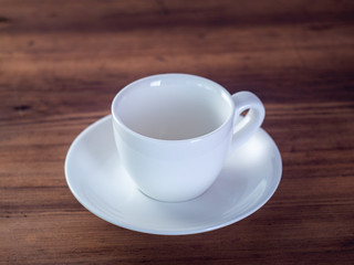 Empty coffee cup on wooden table, close up view. White cup and saucer on brown table. Colourful background. Selective soft focus. Blurred background