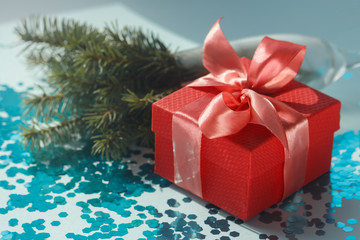 Stylish festive composition with a red gift box with a satin coral bow, Christmas tree branches and blue sprinkled confetti. Hard light and beautiful shadows.Trendy christmas lifestyle blog decoration