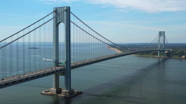 Aerial view of the Verrazano Bridge as the drone camera pans right viewing Staten Island and the waters below on a sunny morning, orbit 1
