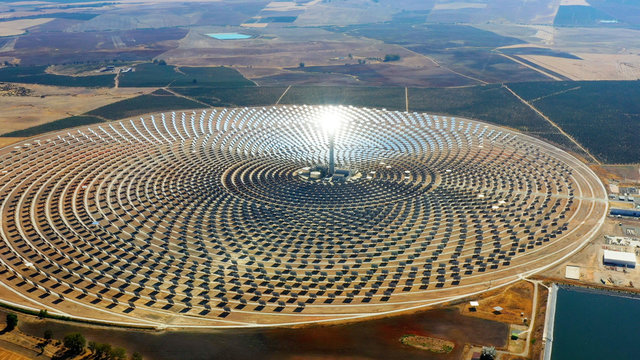 Solar panels in a large thermal circular power plant with the reflection of the sunlight in the panels. Renewable and pollution-free energy in a solar farm in Spain- aerial view with a drone - environ