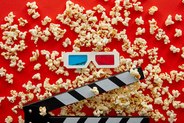 top view of delicious popcorn scattered on red background near clapper board and 3d glasses
