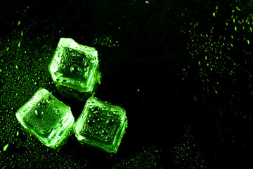 Green ice cubes on black wet table.