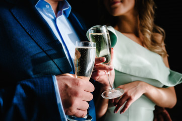 The bride and groom holds a glass of champagne and stand in the room. Close up. Holiday. Look at the glasses.