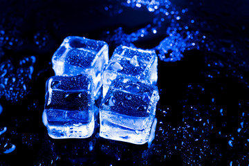 Blue ice cubes on black wet table.
