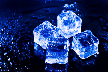 Blue ice cubes on black wet table.